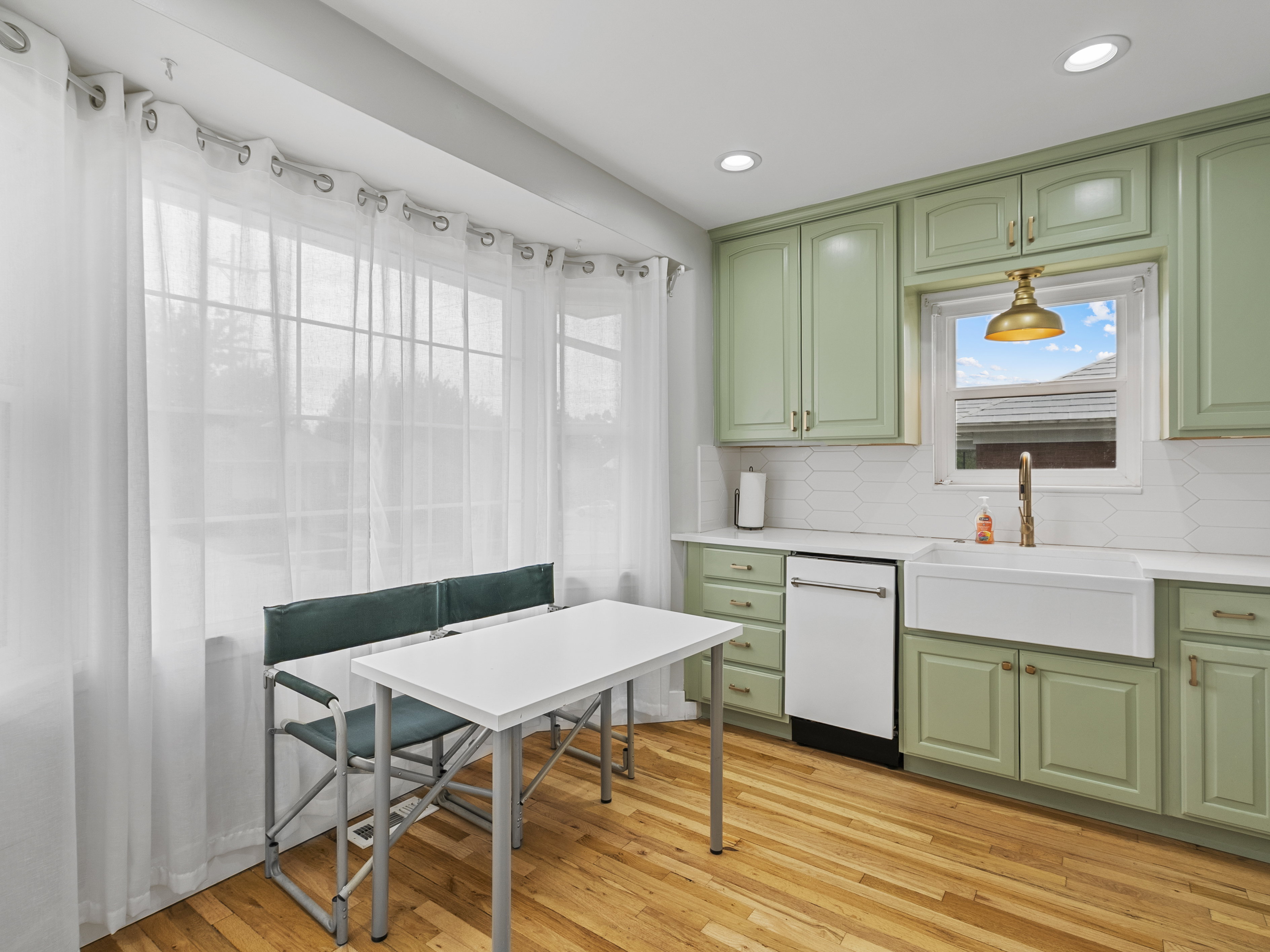 Kitchen featuring wood-finish flooring, light green cabinetry, white countertops, a white subway tile backsplash, and a white farmhouse sink