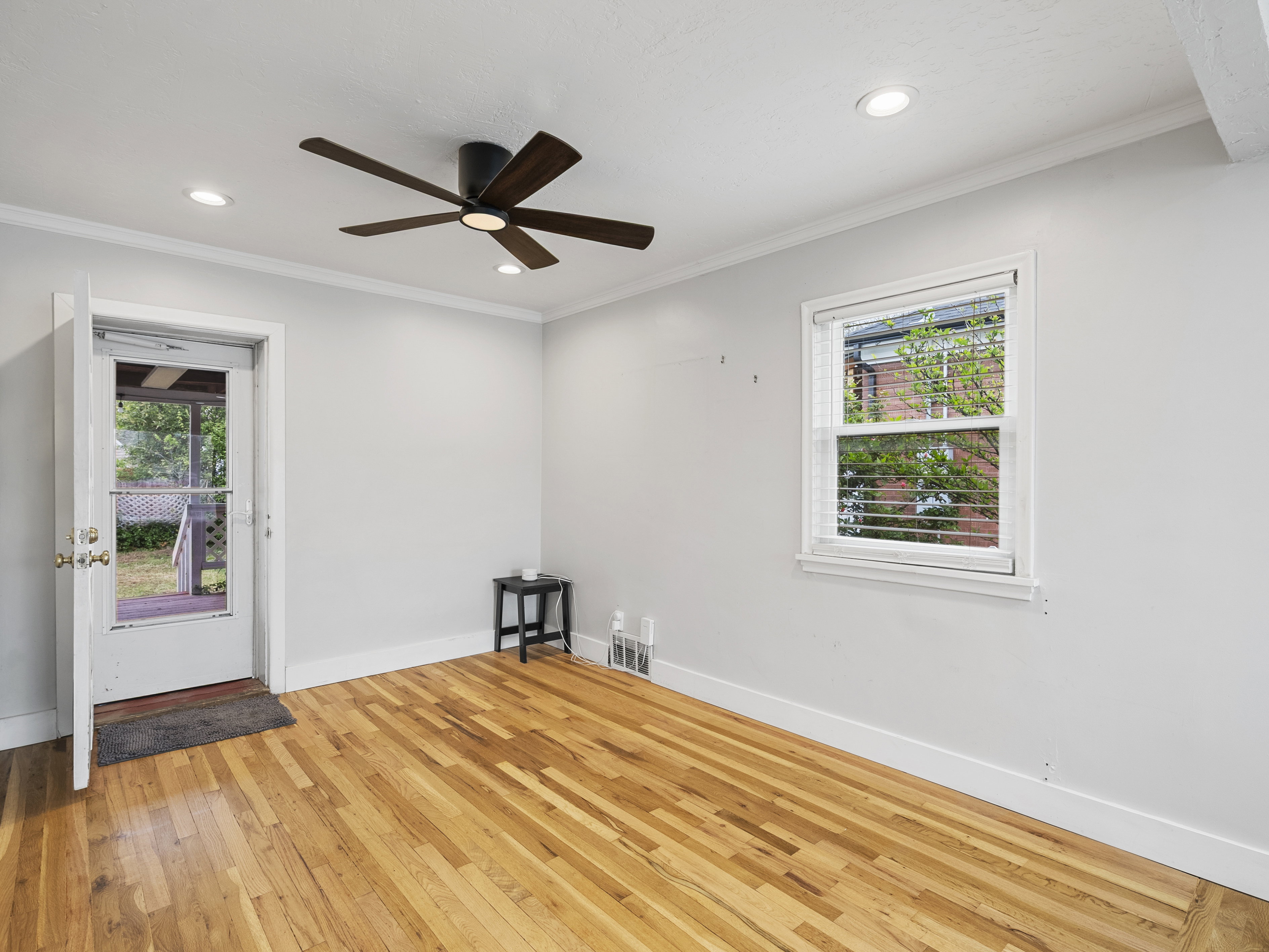 Wood-finish flooring throughout, featuring a ceiling fan with integrated lighting, recessed overhead lighting, and a white-framed window with horizontal blinds