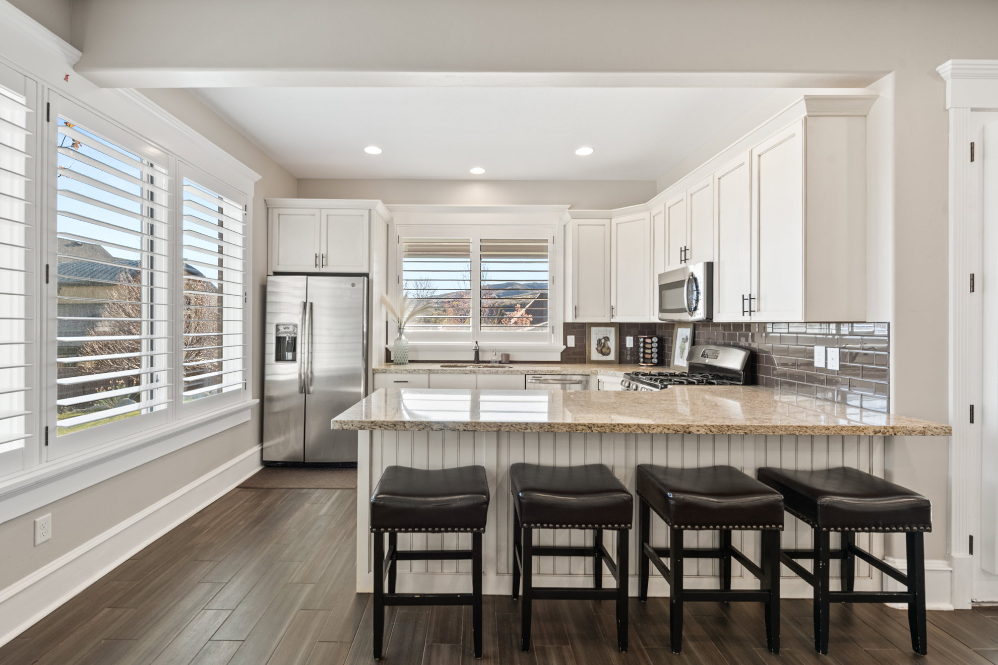 Open-concept kitchen featuring white shaker-style cabinetry, stainless steel appliances, and a breakfast bar with a light-toned countertop