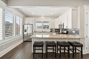 Open-concept kitchen featuring white shaker-style cabinetry, stainless steel appliances, and a breakfast bar with a light-toned countertop
