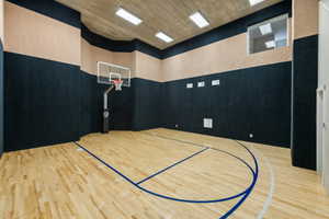 Indoor gymnasium featuring a full basketball court with wood-finish flooring, a mounted basketball hoop, and padded wall surfaces