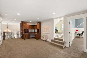 Expansive carpeted loft area featuring a built-in wood-finish desk with integrated shelving, recessed lighting, and a wrought iron banister overlooking the floor below