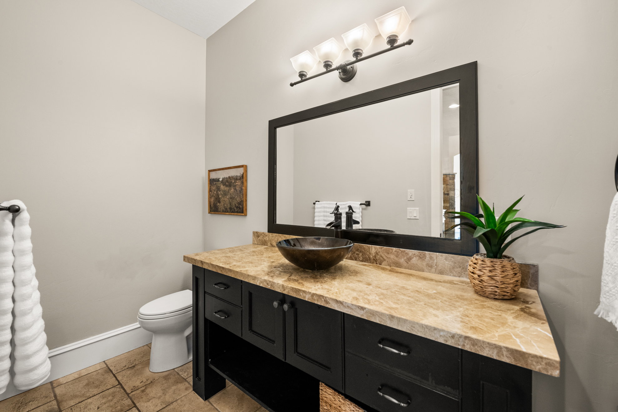 Powder room featuring a dark wood vanity with a vessel sink, a light-toned stone countertop, and a large framed mirror