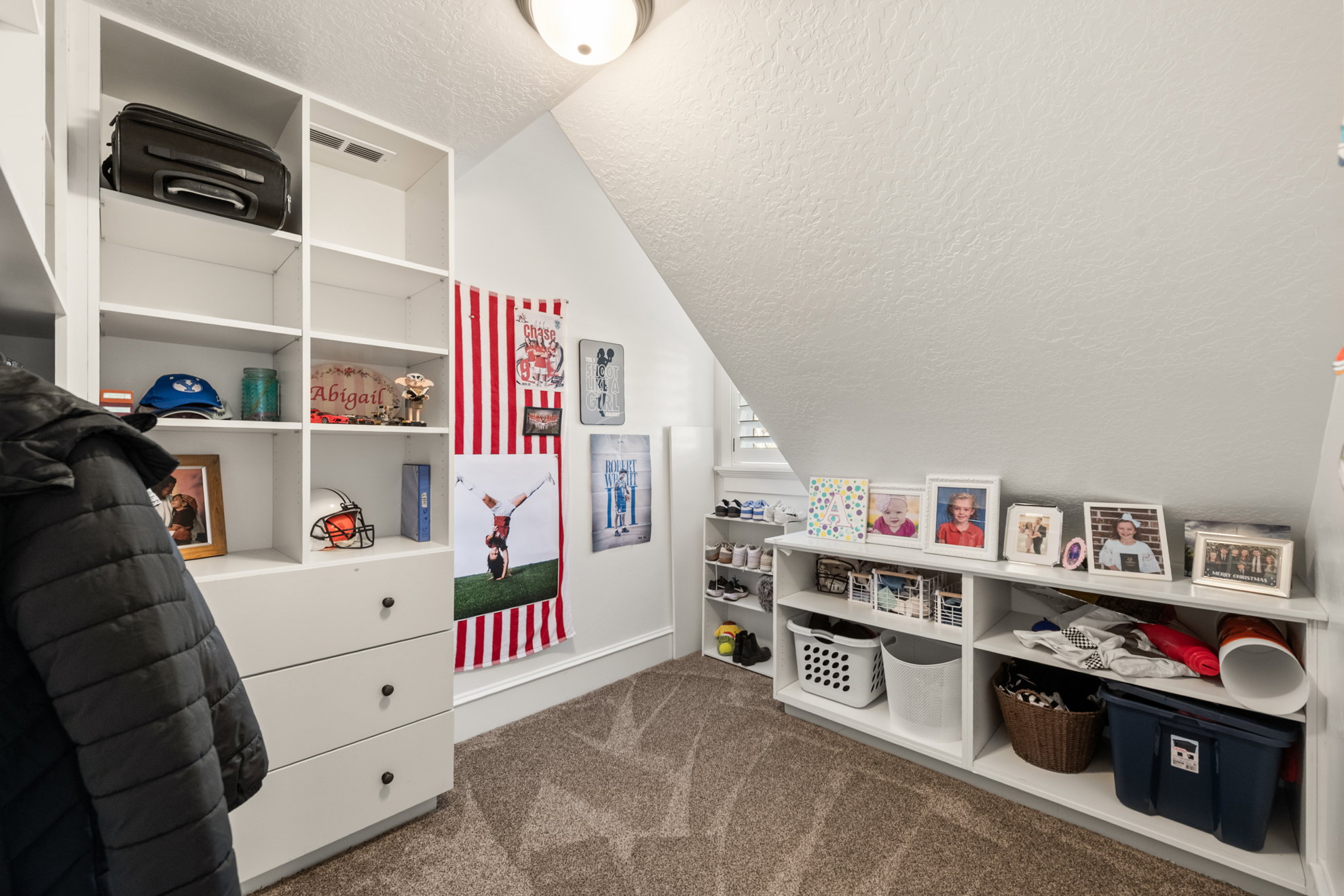 Carpeted bonus room featuring built-in white shelving, integrated drawers with dark hardware, and a window with white shutters