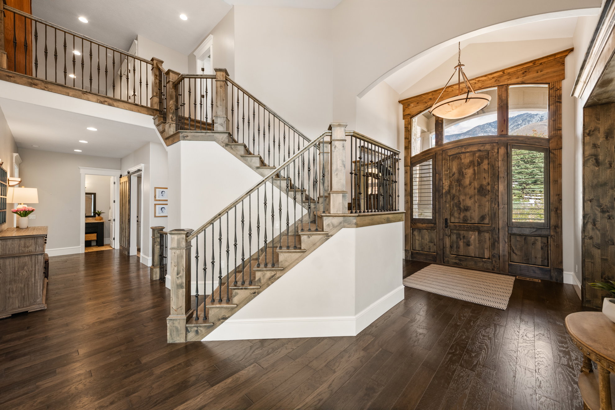 Grand foyer featuring dark wood-finish flooring, a double-height ceiling, and a prominent staircase with wrought iron balusters