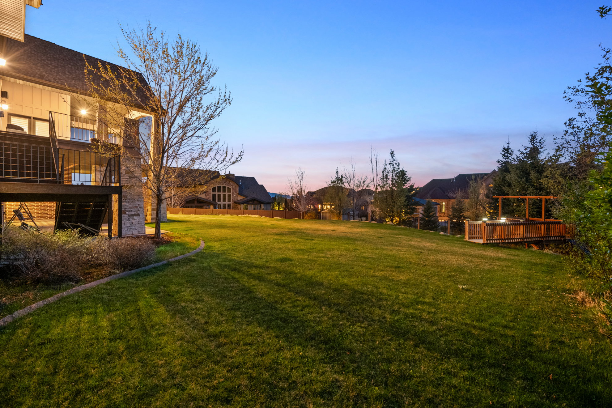 Expansive lawn area featuring a multi-level deck with black railings, a stone chimney, and a wooden hot tub deck with an overhead pergola structure