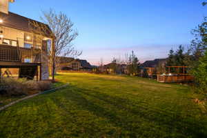 Expansive lawn area featuring a multi-level deck with black railings, a stone chimney, and a wooden hot tub deck with an overhead pergola structure