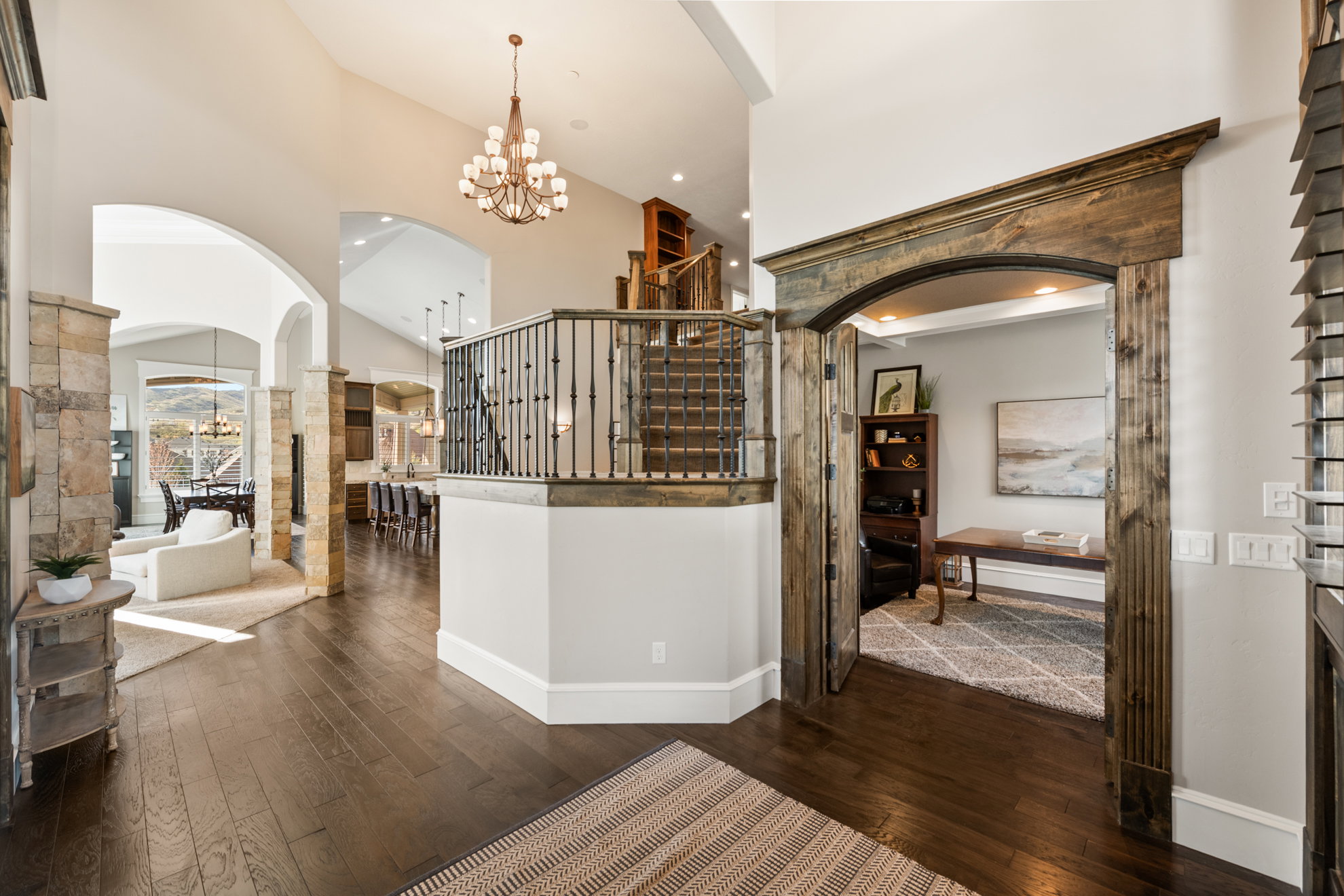 Spacious foyer with dark wood-finish flooring, a grand staircase featuring wood and iron railings, and a vaulted ceiling with a chandelier