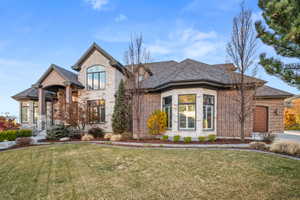 Stone and brick exterior featuring a prominent arched entry, multiple gables, a bay window with plantation shutters, a wood-finish garage door, and a manicured front lawn with mature landscaping
