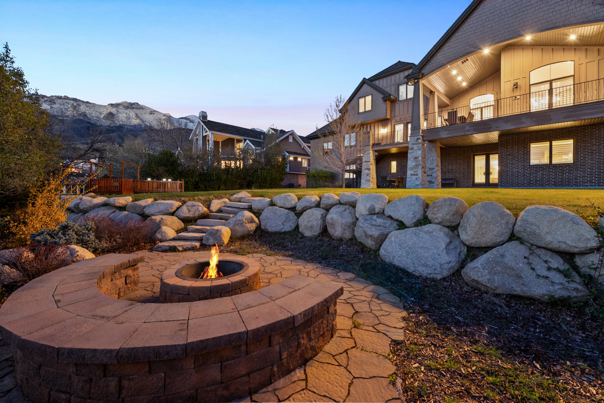 Expansive backyard featuring a built-in stone fire pit with curved seating, flagstone pathway, and rock retaining walls