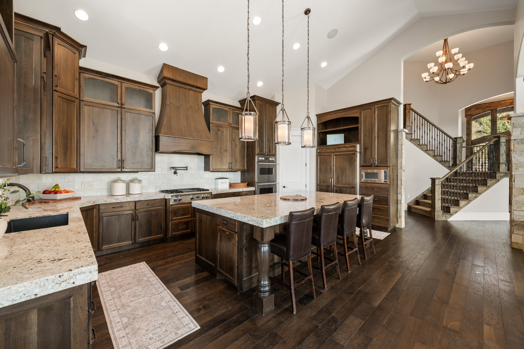 Gourmet kitchen featuring a large central island with seating, dark wood-finish cabinetry, light-colored countertops, stainless steel appliances, and a tile backsplash
