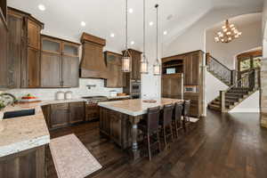 Gourmet kitchen featuring a large central island with seating, dark wood-finish cabinetry, light-colored countertops, stainless steel appliances, and a tile backsplash