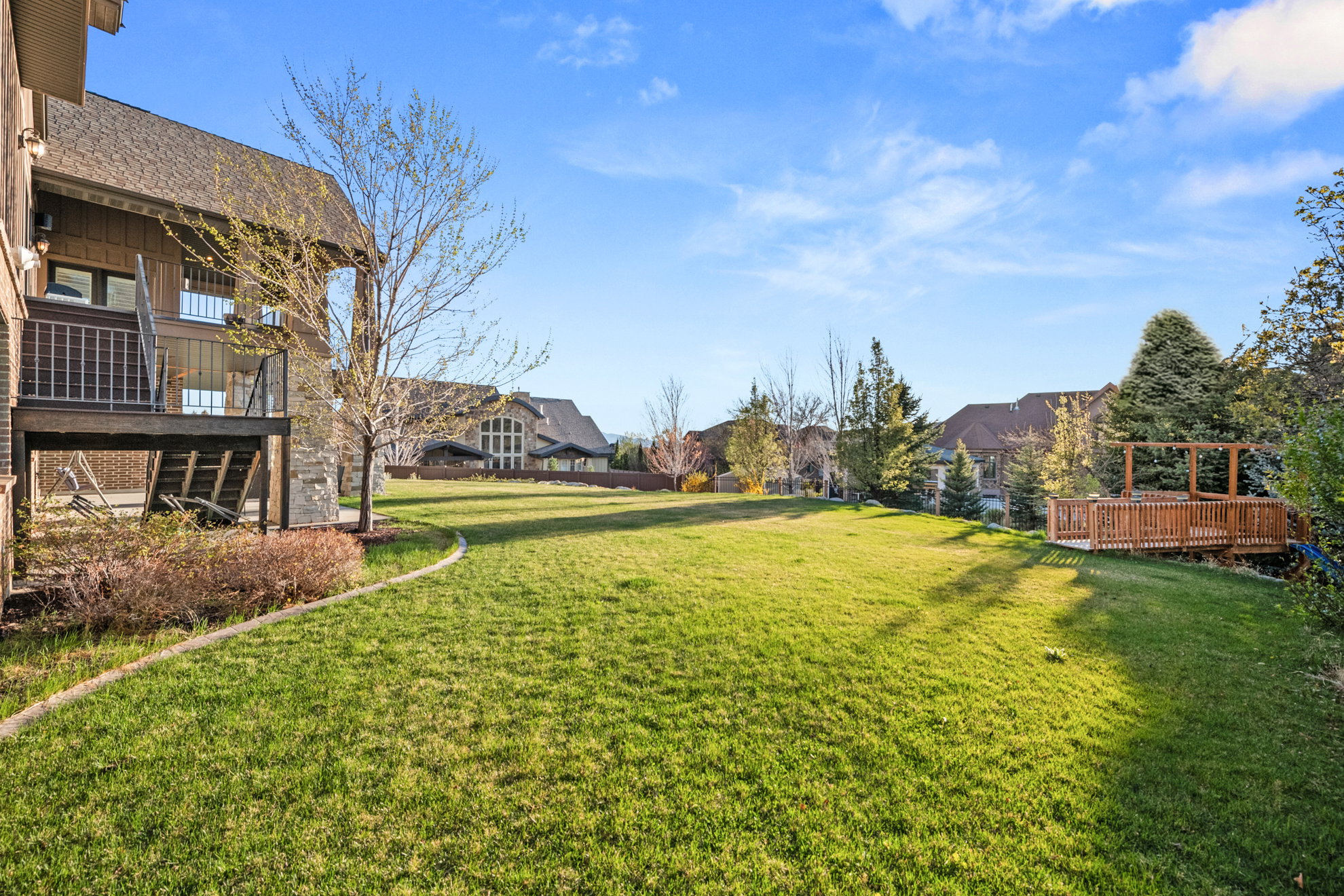 Expansive rear lawn featuring a wooden deck with a pergola, mature trees, and a terraced backyard