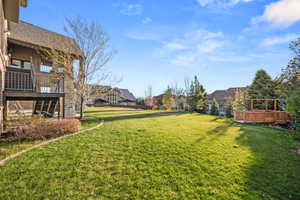 Expansive rear lawn featuring a wooden deck with a pergola, mature trees, and a terraced backyard