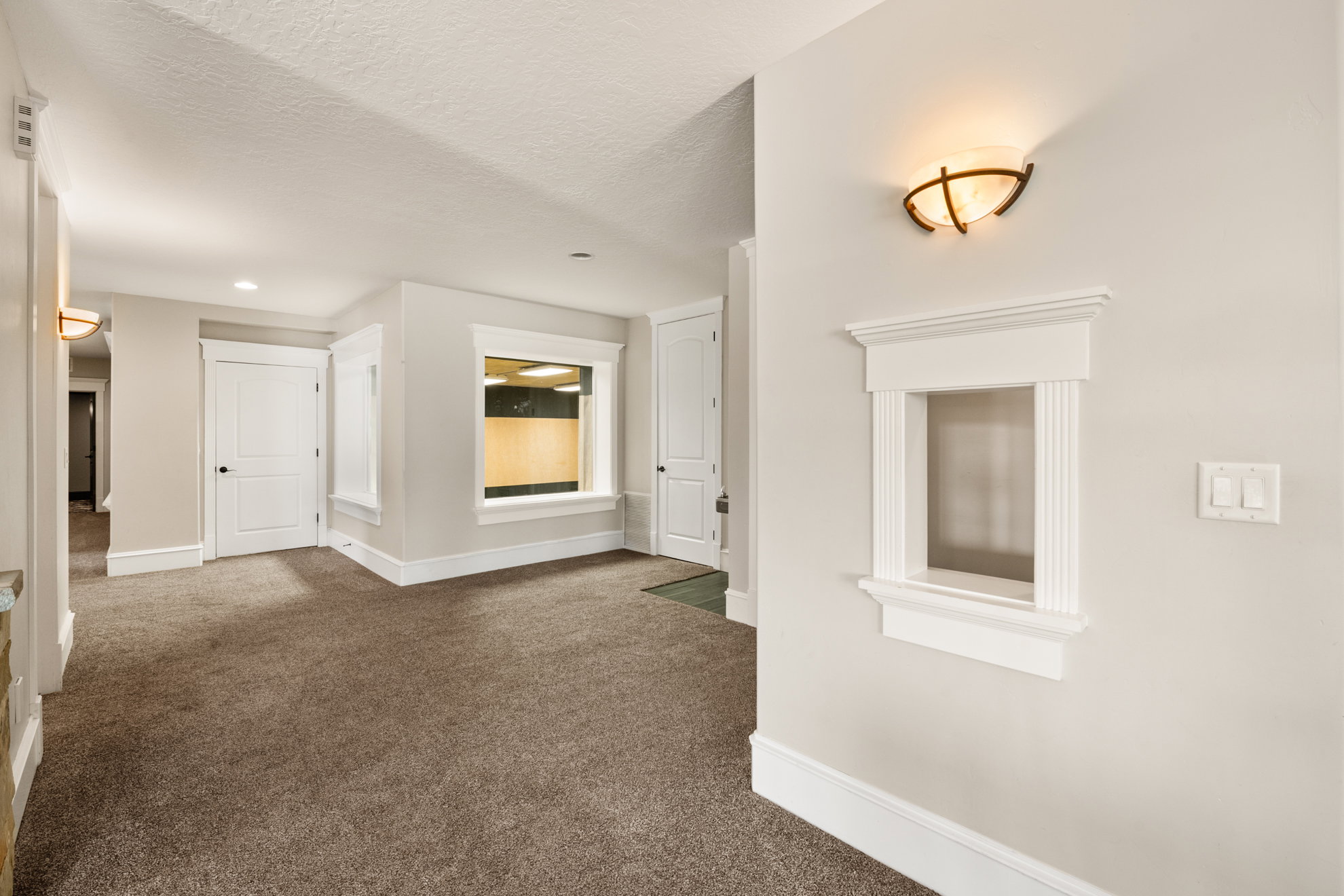 Interior wall with decorative pass-through window, sconce lighting, and light-toned carpet flooring
