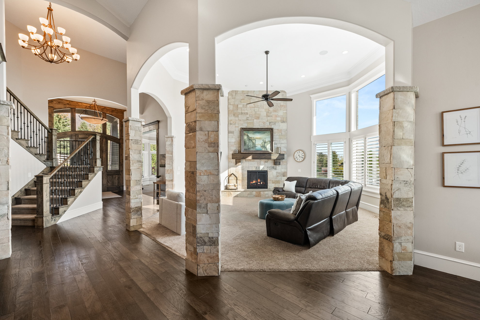 Expansive living area with wood-finish flooring, stone-clad archways, and a multi-level staircase with wrought iron balusters