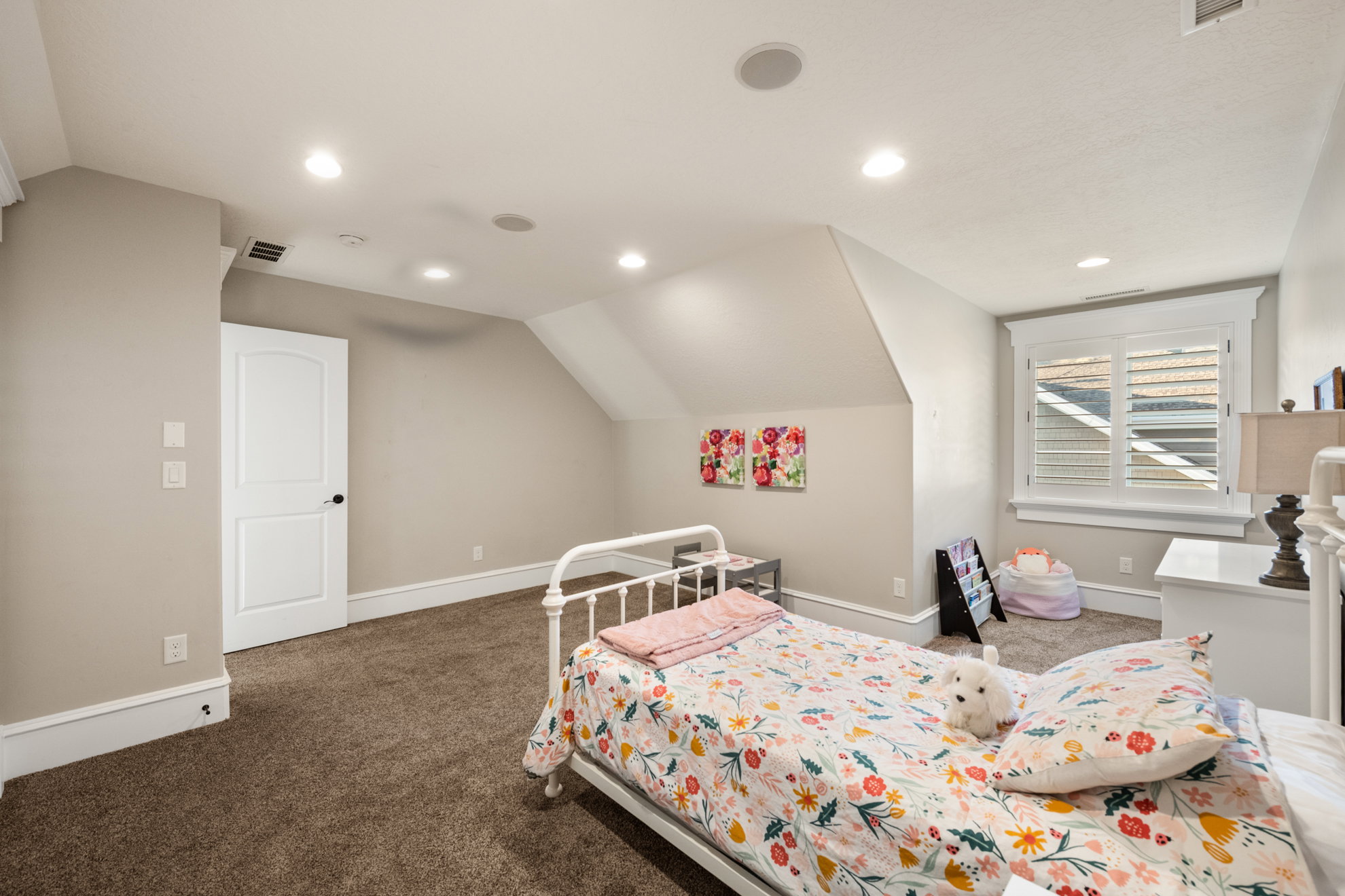 Carpeted interior room featuring a white paneled door, recessed ceiling lighting, and a window with plantation shutters