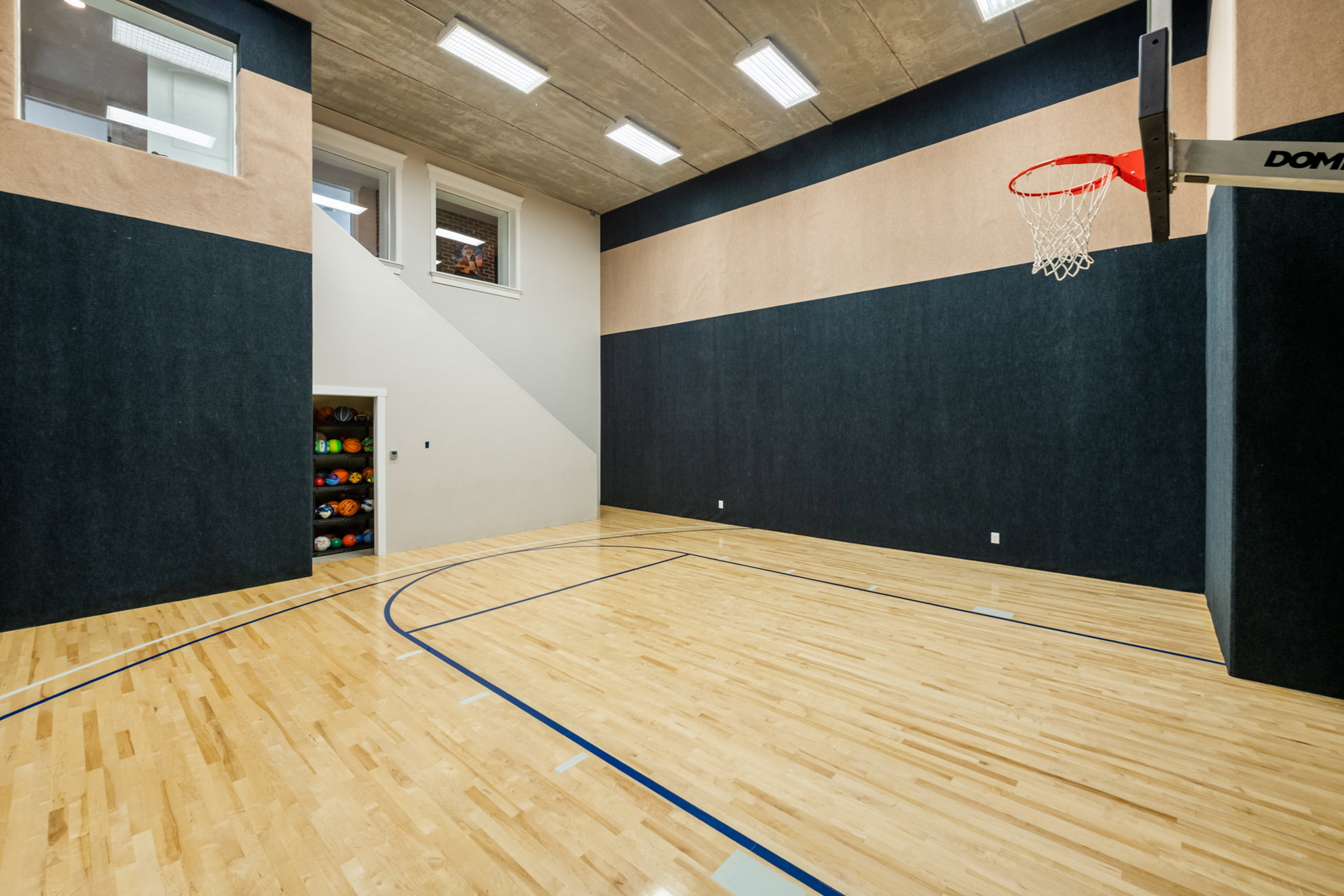 Indoor basketball court featuring light wood flooring with regulation markings, a professional-grade hoop, and sound-absorbing wall panels
