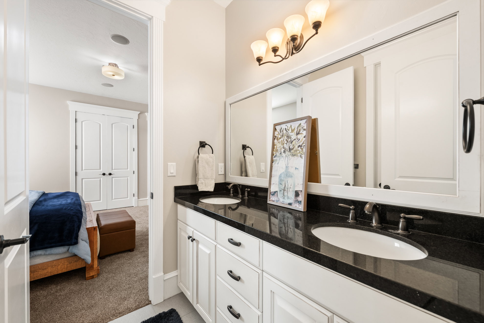 Dual vanity featuring a dark countertop, white cabinetry with dark hardware, and two undermount sinks