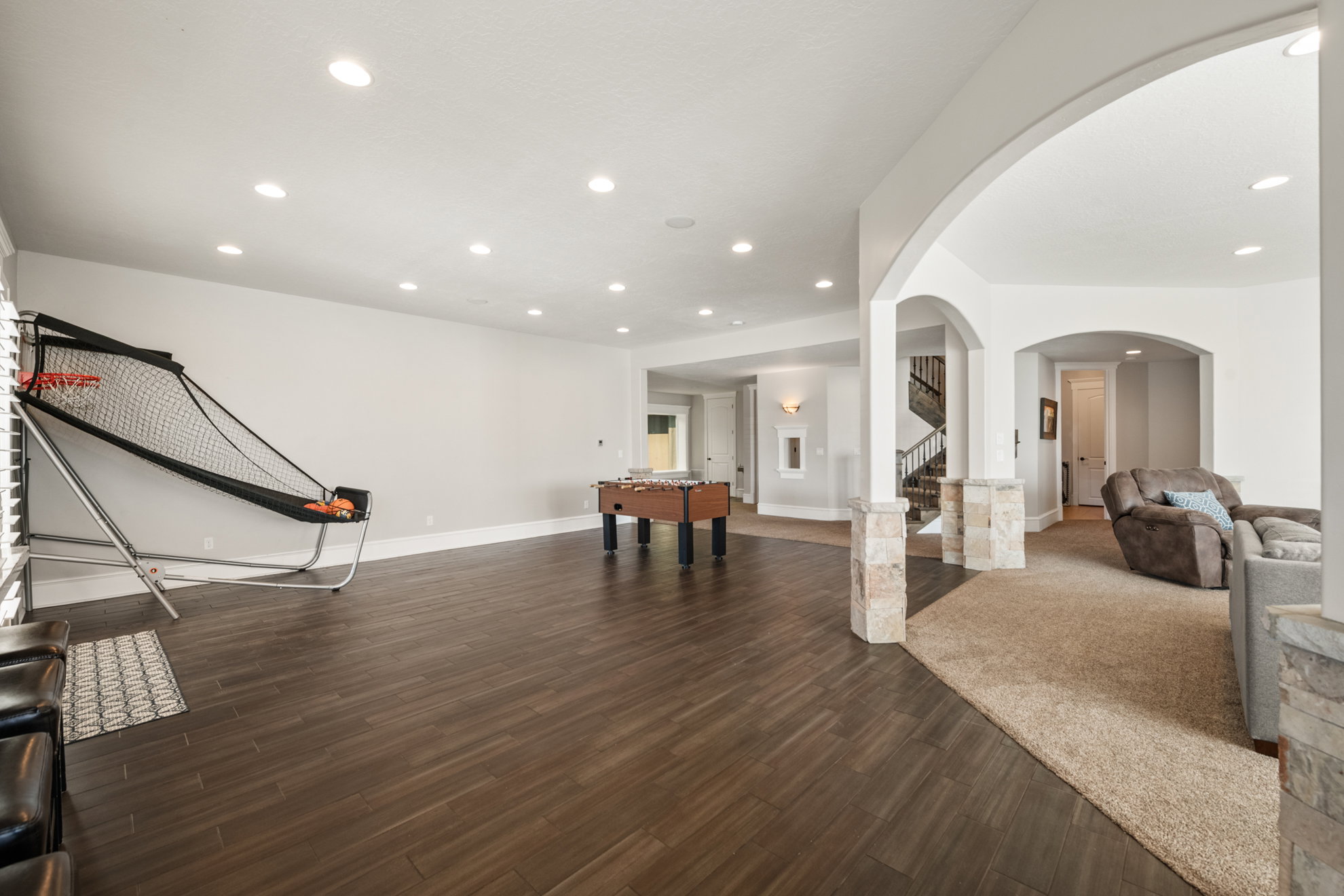 Spacious lower level featuring wood-finish flooring, recessed lighting, arched doorways, and stone-clad columns