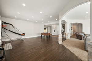 Spacious lower level featuring wood-finish flooring, recessed lighting, arched doorways, and stone-clad columns