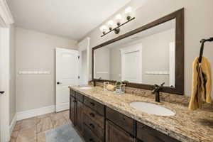 Double vanity featuring a granite countertop, dual undermount sinks, and dark wood cabinetry