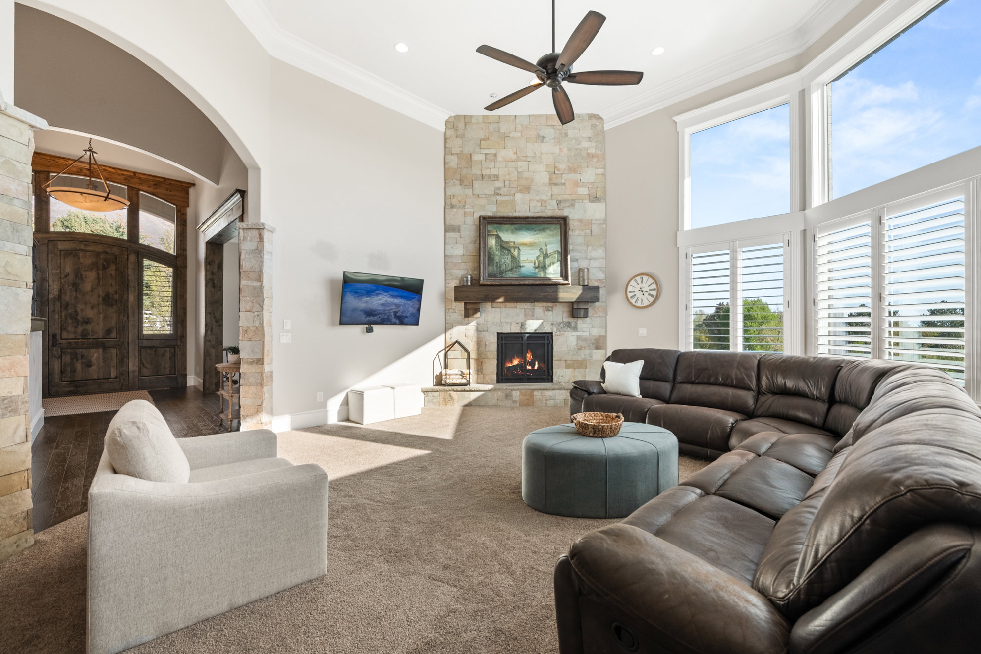 Spacious living area featuring a floor-to-ceiling stone fireplace with a wood mantle, high vaulted ceilings, and a ceiling fan