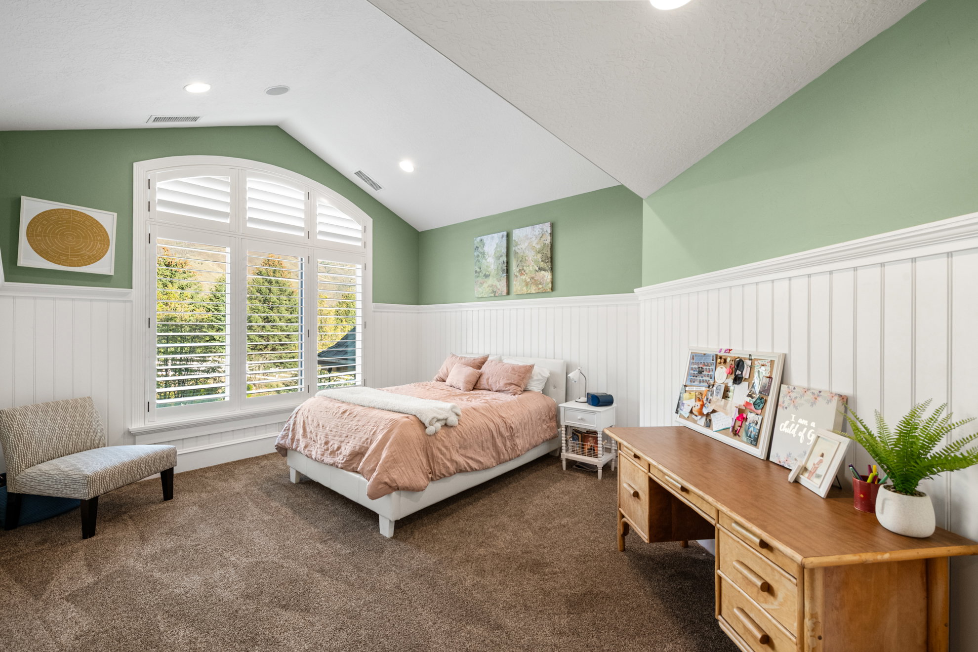 Spacious room featuring vaulted ceilings, recessed lighting, arched window with plantation shutters, wainscoting, and carpeted flooring