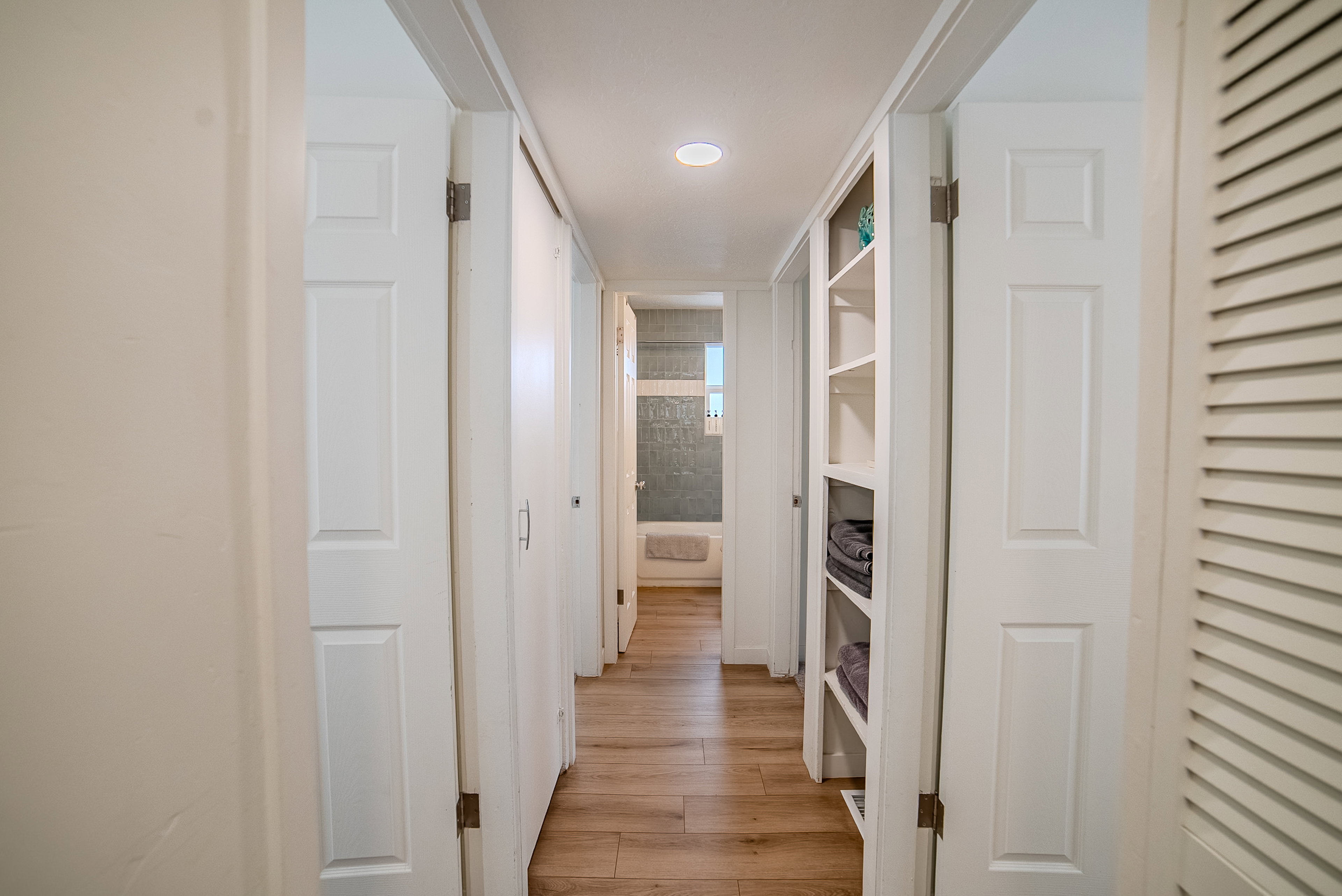Hallway featuring wood-finish flooring, recessed lighting, white paneled doors, and a built-in shelving unit
