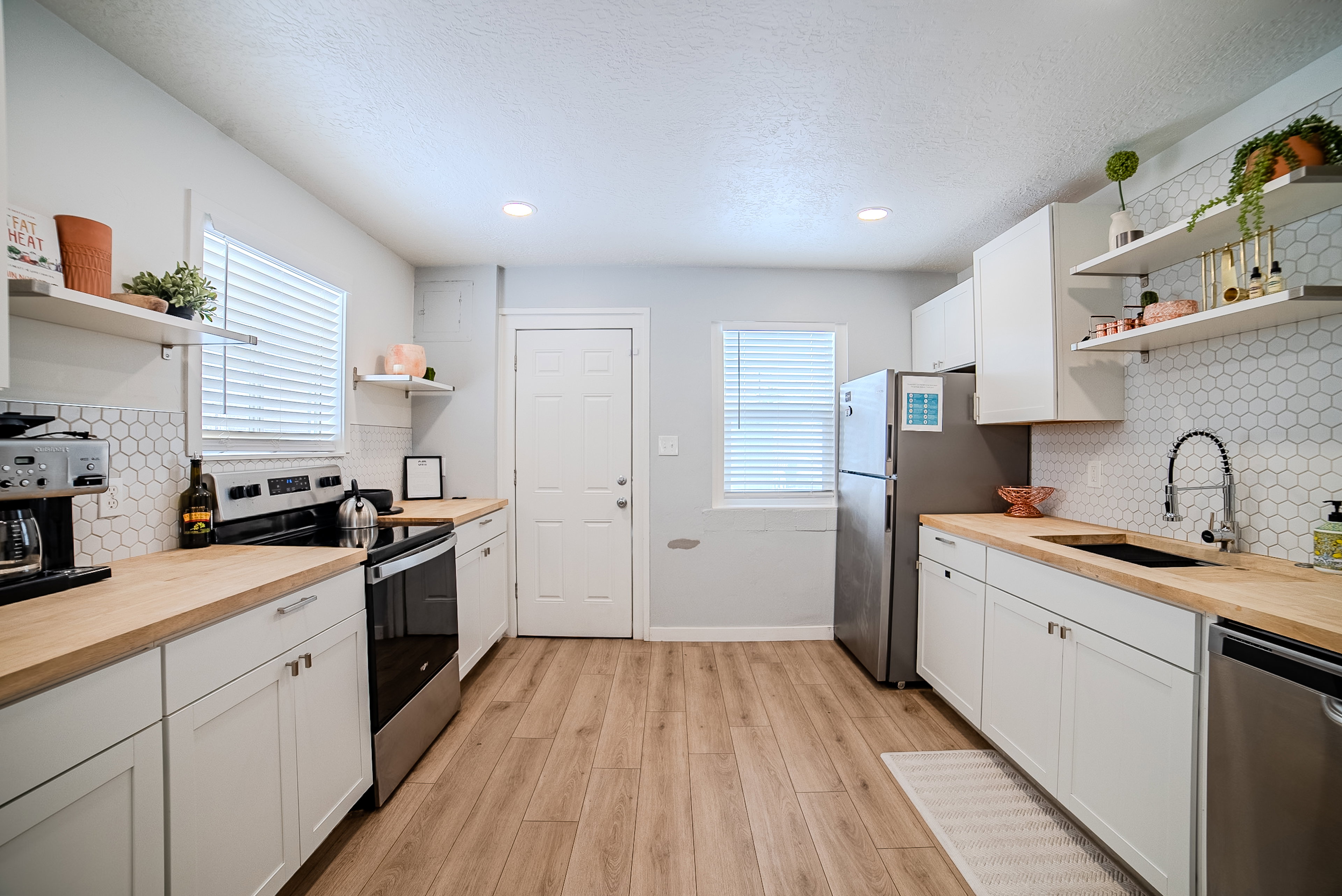 Kitchen featuring white shaker-style cabinetry, wood-finish countertops, hexagon tile backsplash, stainless steel appliances, and wood-finish flooring