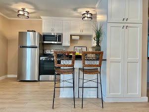 Kitchen featuring white shaker-style cabinetry, stainless steel appliances, a black countertop, and wood-finish flooring