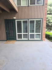 Patio entrance featuring a dark green paneled door with glass inserts, adjacent to two large windows fitted with white plantation shutters