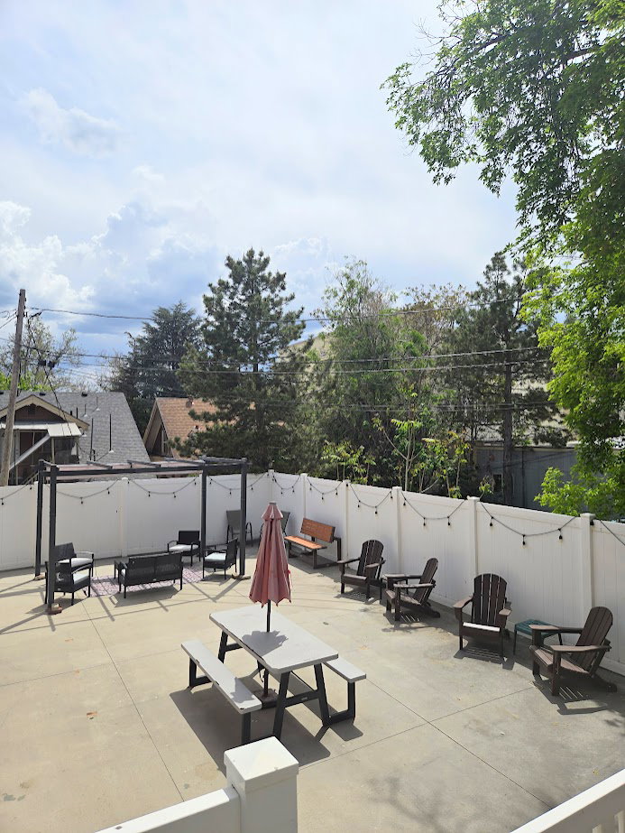 Paved patio space featuring a white privacy fence, string lighting, and a dark-toned pergola