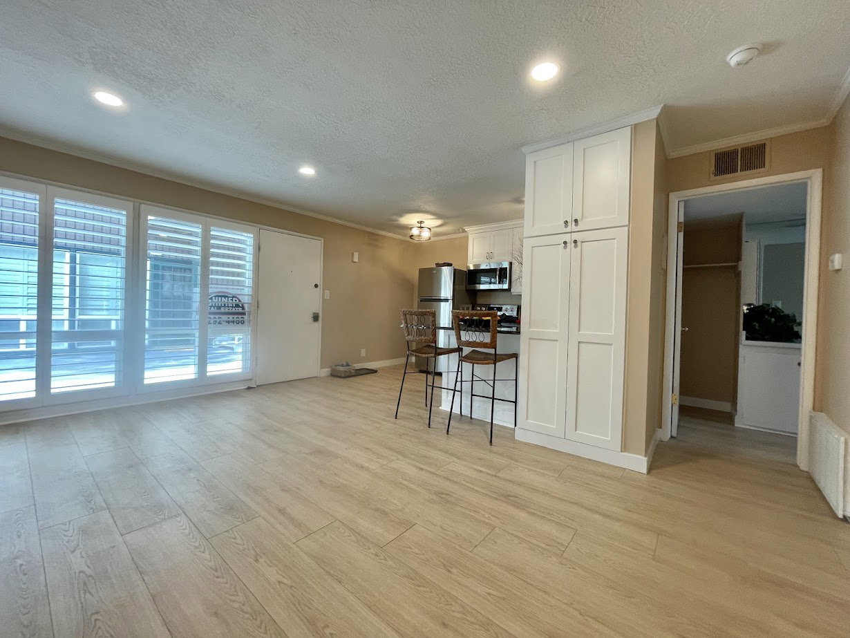 Open-concept living area featuring wood-finish flooring, recessed lighting, and a full wall of sliding glass doors with interior plantation shutters