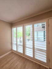 Triple window unit featuring white plantation shutters, wood-finish flooring, crown molding, and neutral wall tones