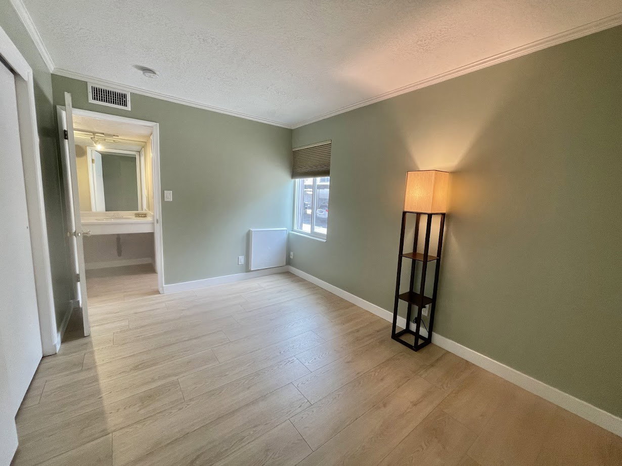 Spacious room featuring wood-finish flooring, light green walls, a window with a roller shade, and crown molding