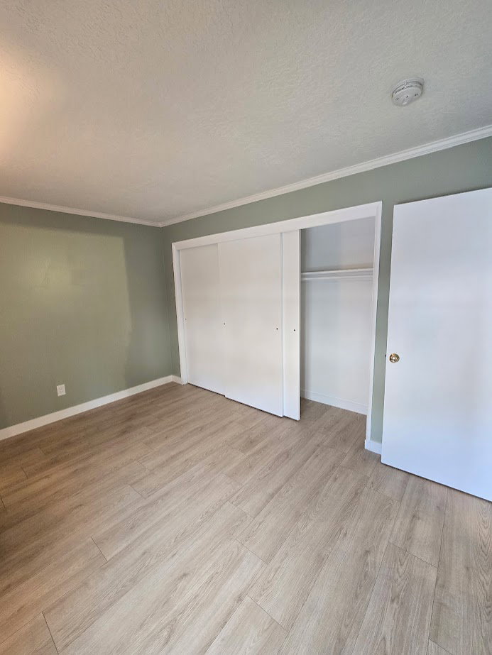 Room featuring wood-finish flooring, light green walls, white baseboards, and white crown molding