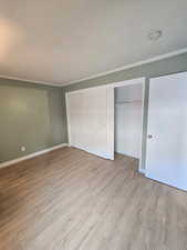 Room featuring wood-finish flooring, light green walls, white baseboards, and white crown molding