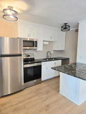 Kitchen featuring white cabinetry, stainless steel appliances, dark granite countertops, and wood-finish flooring