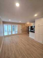 Open-concept living space featuring wood-finish flooring, recessed lighting, and a kitchen with white cabinetry and stainless steel appliances