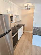 Kitchen featuring stainless steel appliances, dark stone countertops, white cabinetry, a double basin sink with a gooseneck faucet, and wood-finish flooring