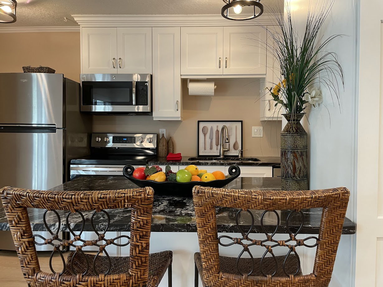 Kitchen featuring white cabinetry, stainless steel appliances, dark granite countertops, and a kitchen island with seating