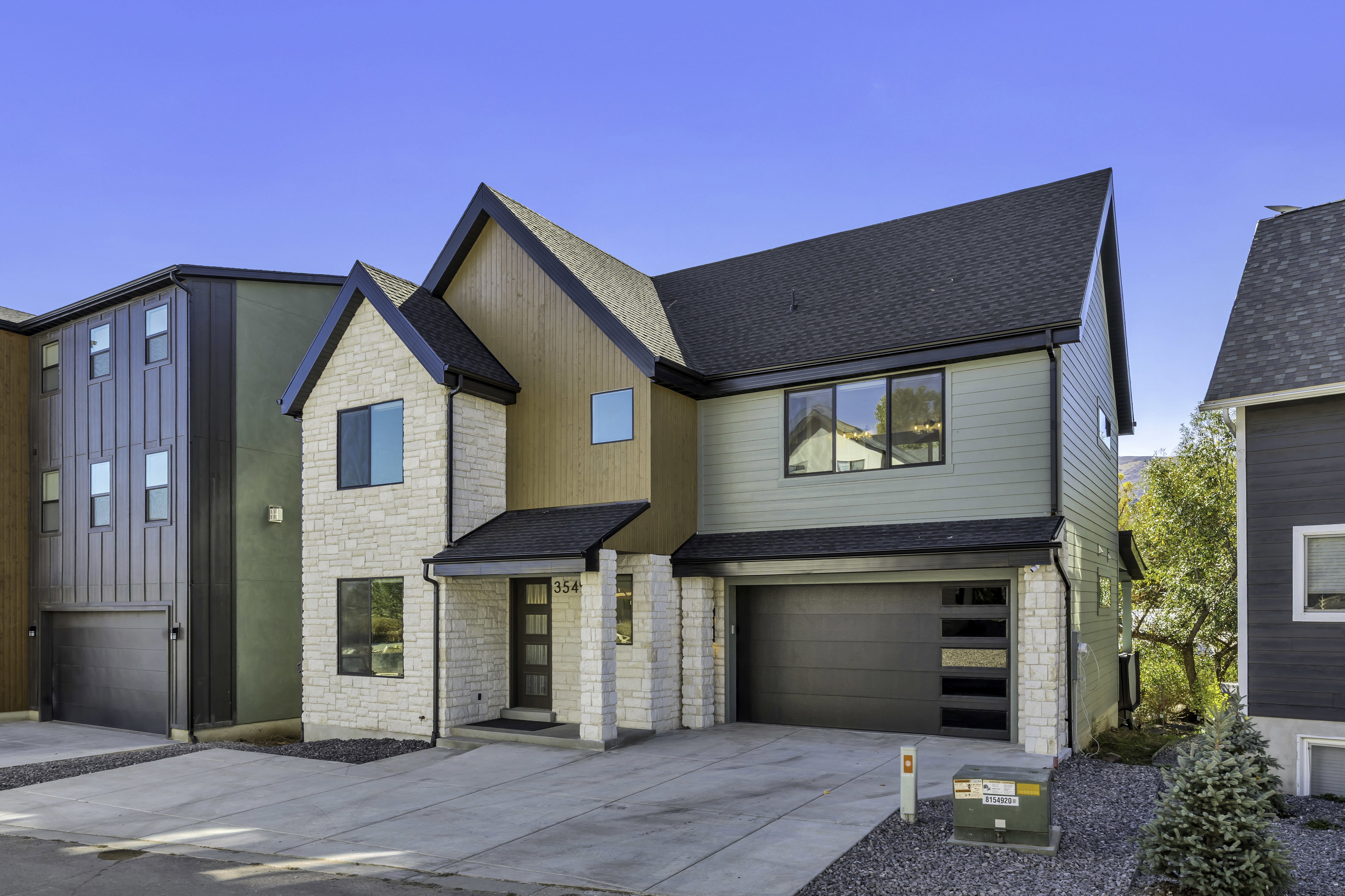 View of front of house with stone siding, an attached garage, a shingled roof, and concrete driveway