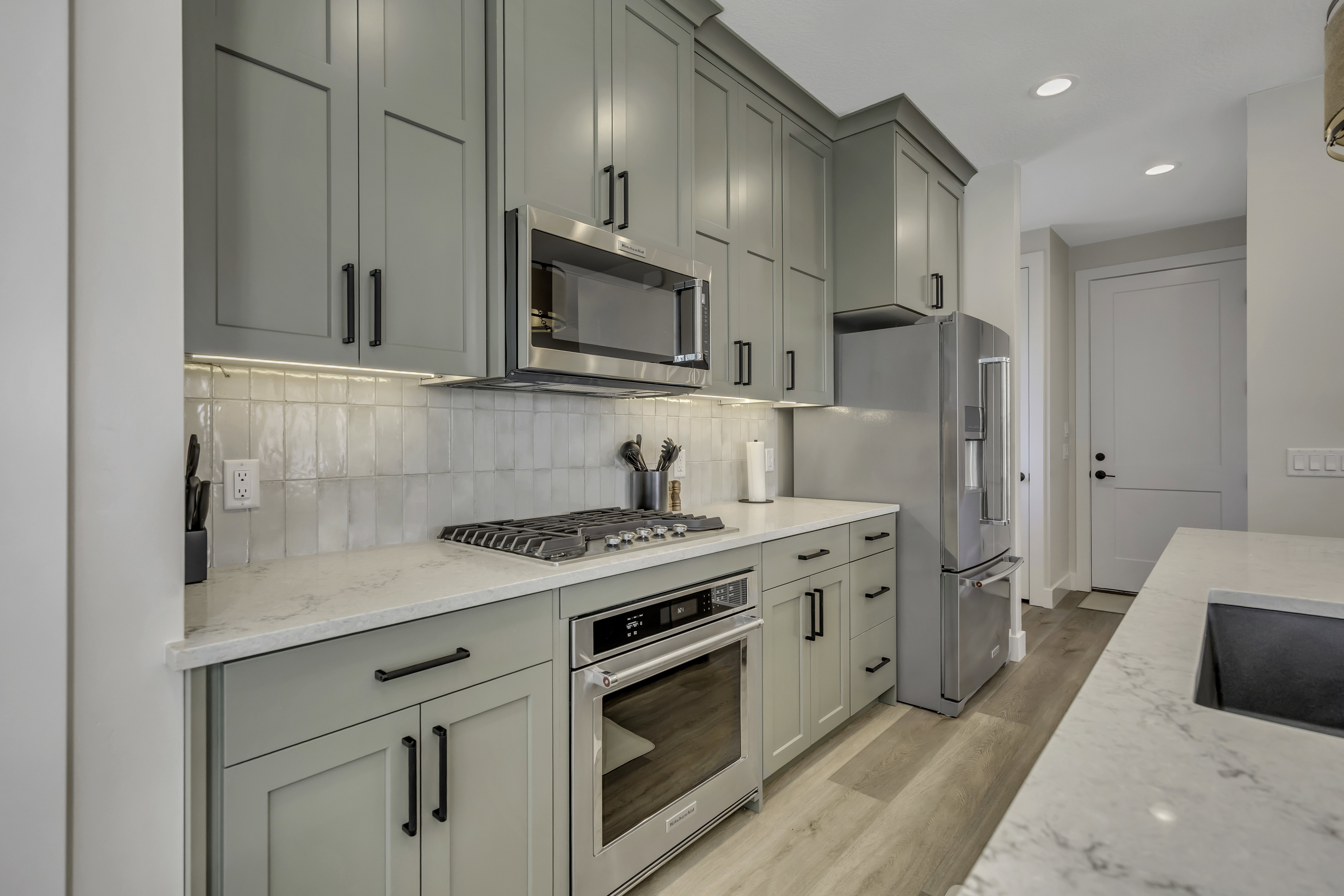 Kitchen with stainless steel appliances, light wood-style flooring, light stone countertops, backsplash, and recessed lighting