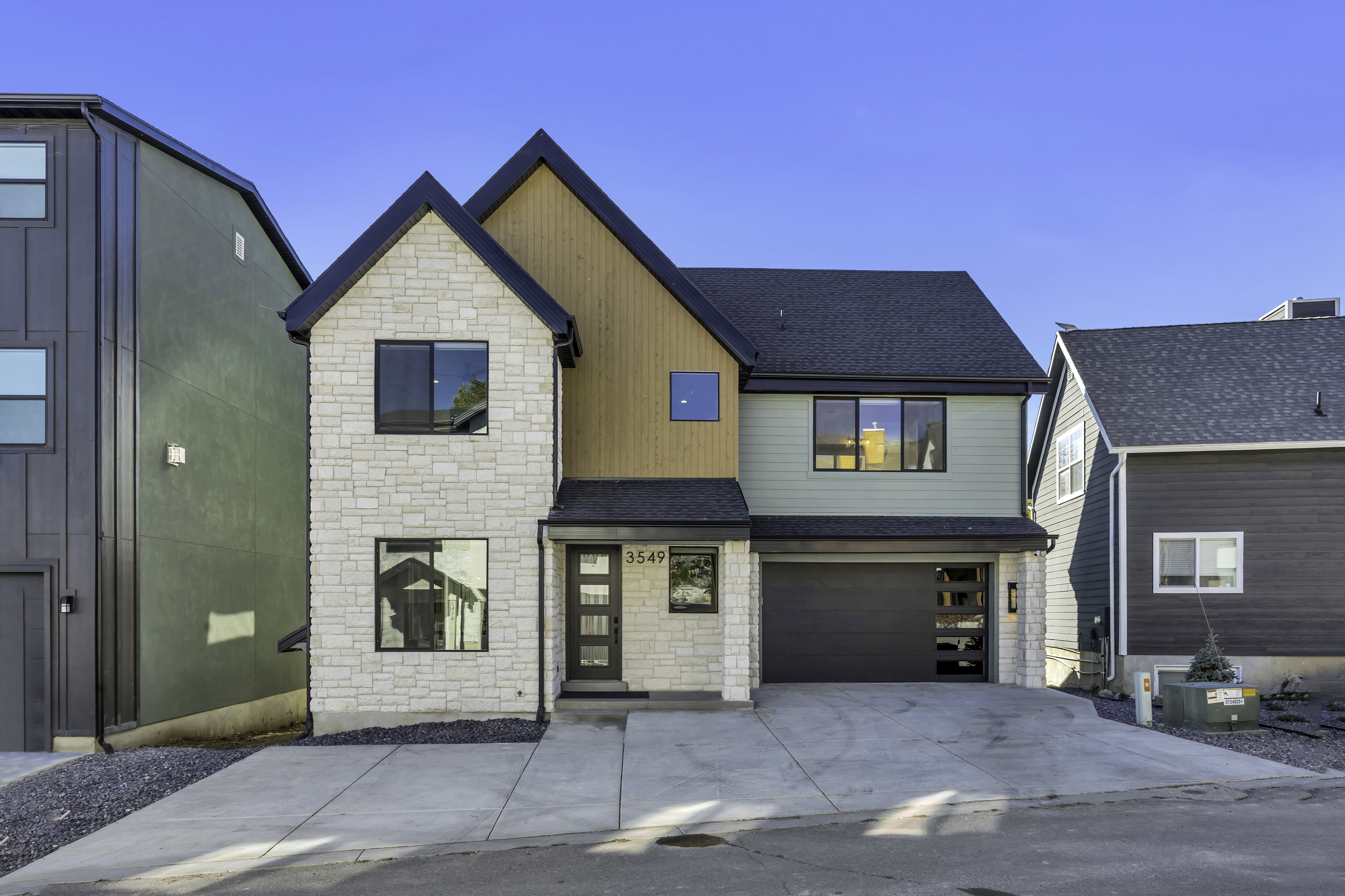 View of front of property with stone siding, an attached garage, a shingled roof, and driveway