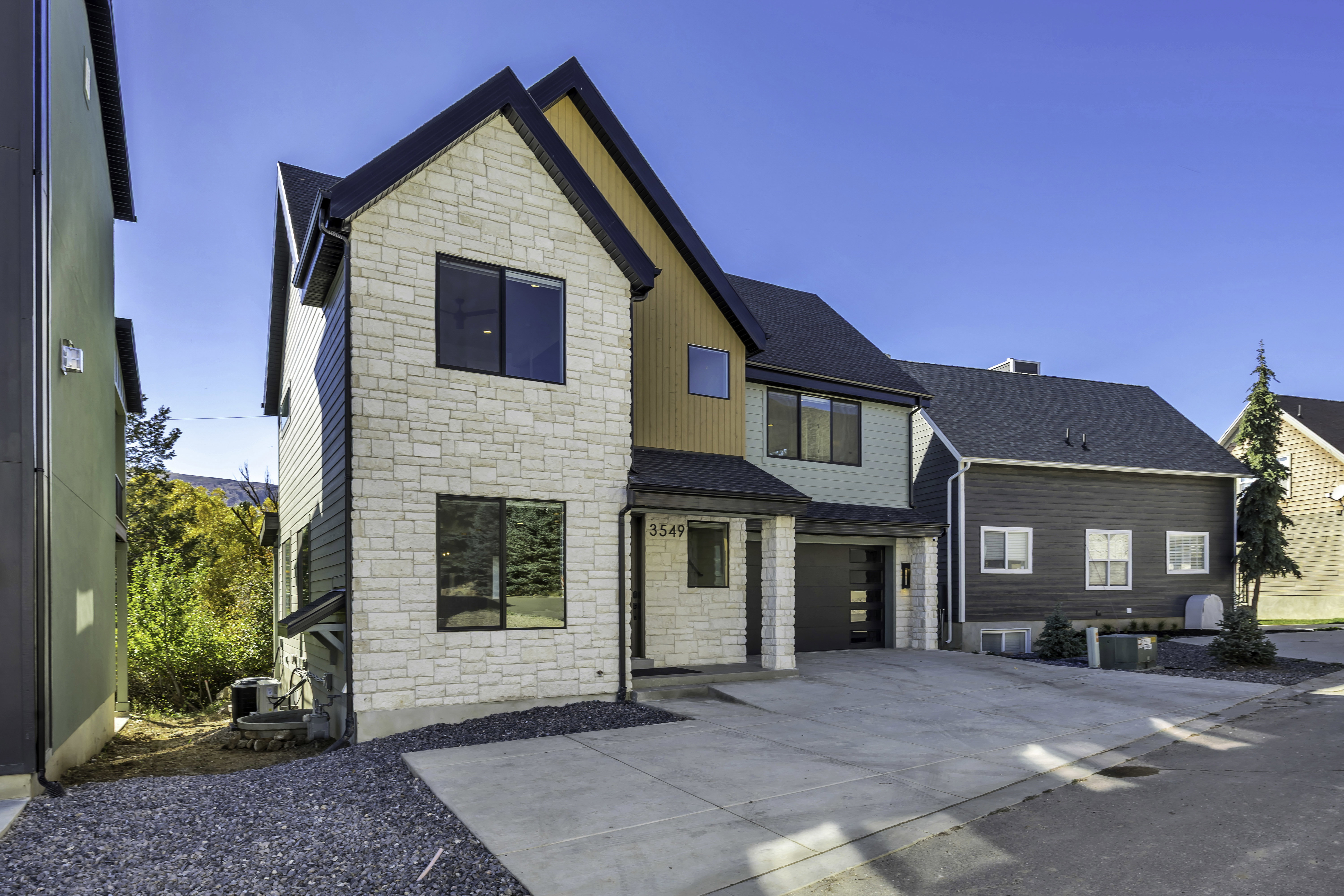 View of front of home featuring stone siding, board and batten siding, driveway, a shingled roof, and a garage