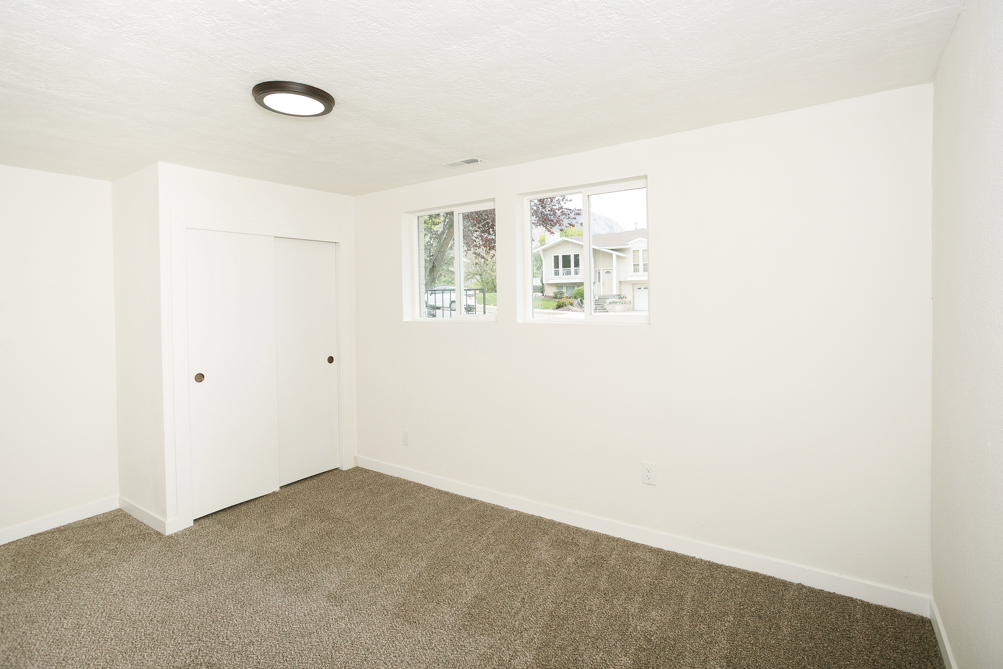Carpeted room featuring white walls, a built-in closet with sliding doors, two windows, and a flush-mount ceiling light fixture
