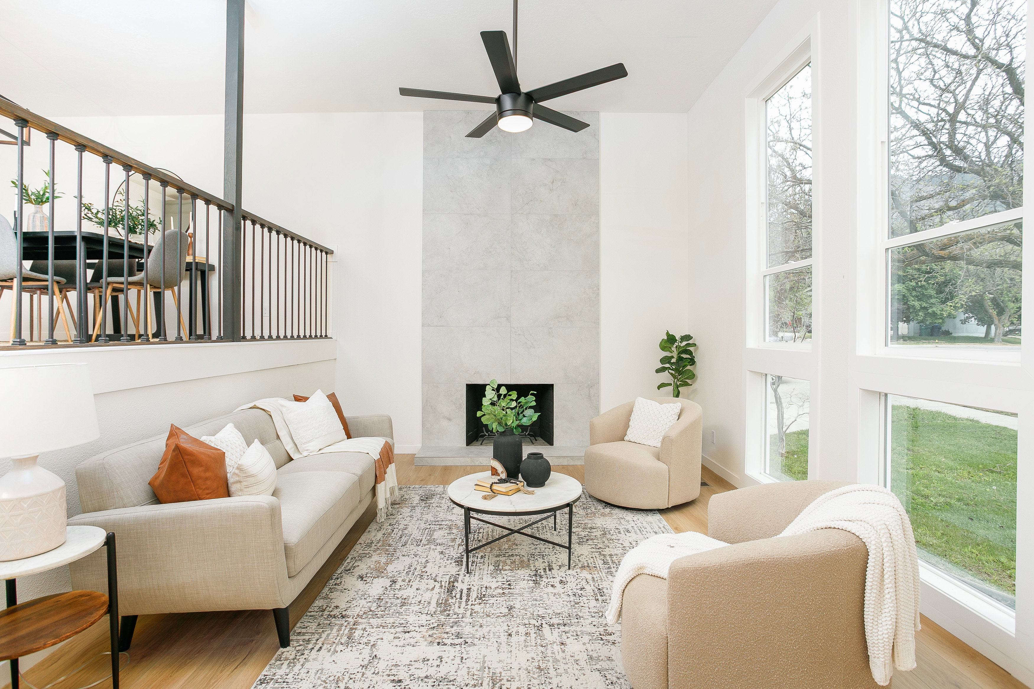 Open-concept living space featuring a floor-to-ceiling fireplace with stone-finish surround, high ceilings, wood-finish flooring, and a contemporary ceiling fan