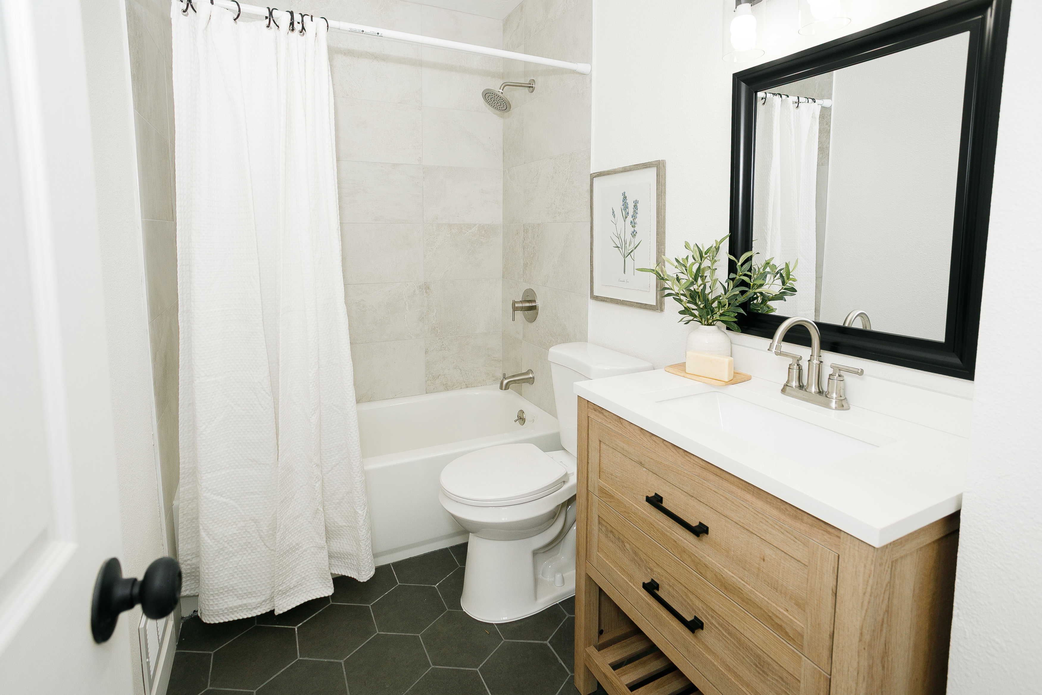 Bathroom featuring a wood-finish vanity with a white countertop and integrated sink, a rectangular framed mirror, and hexagon tile flooring