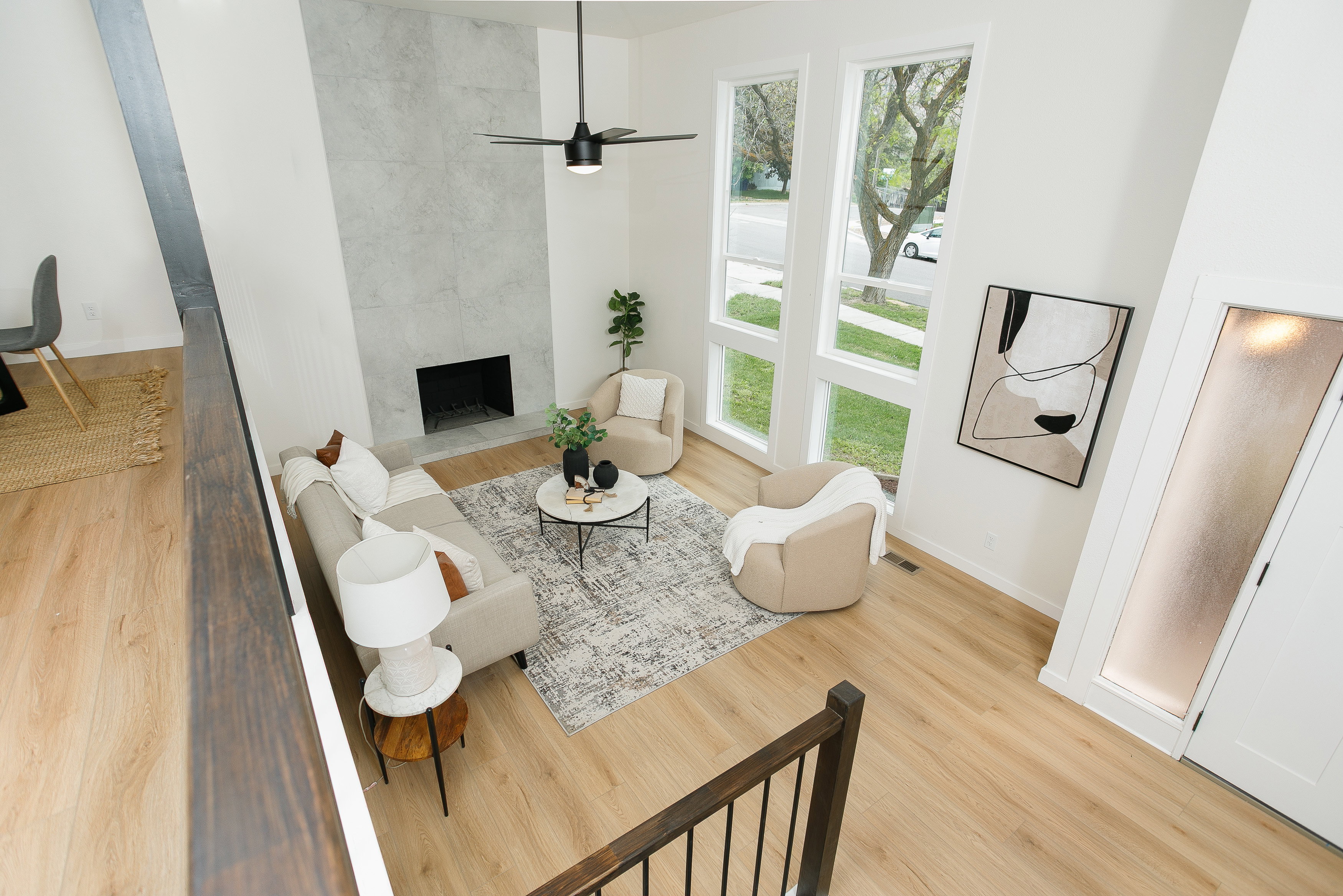 Living area featuring soaring ceilings, a tiled fireplace, wood-finish flooring, a modern ceiling fan, and large windows